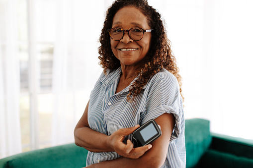 Portrait of a woman using continuous glucose monitoring to manage her diabetes at home. Mature woman using the latest health technology to measure and keep her blood glucose levels under control.